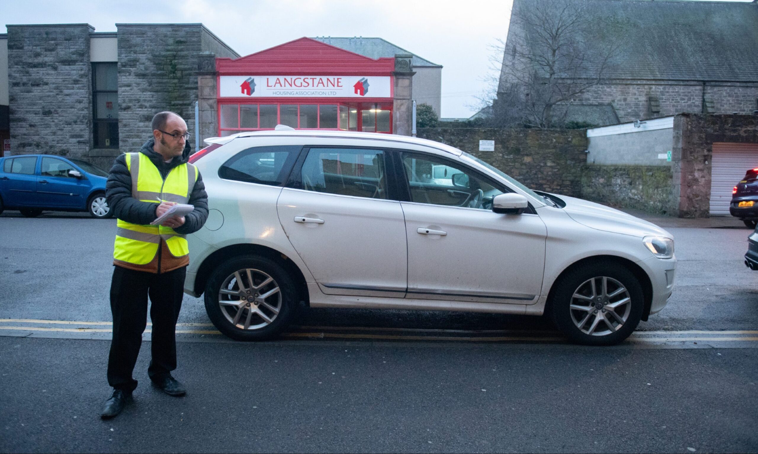 Reporter David Mackay writing in notepad next to parked car on double yellow lines. 