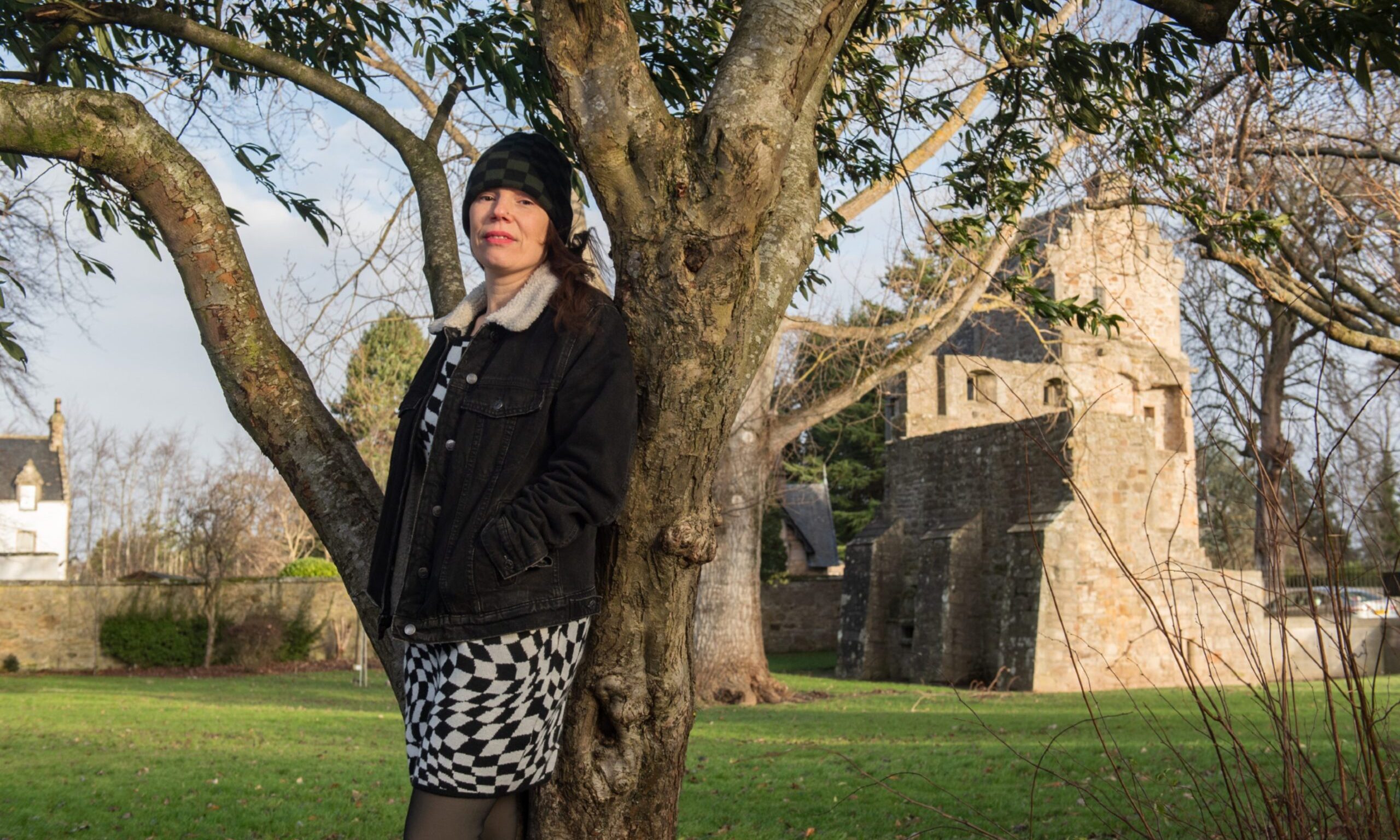 Kellie Lawtie leaning against tree with Elgin Cathedral behind. 