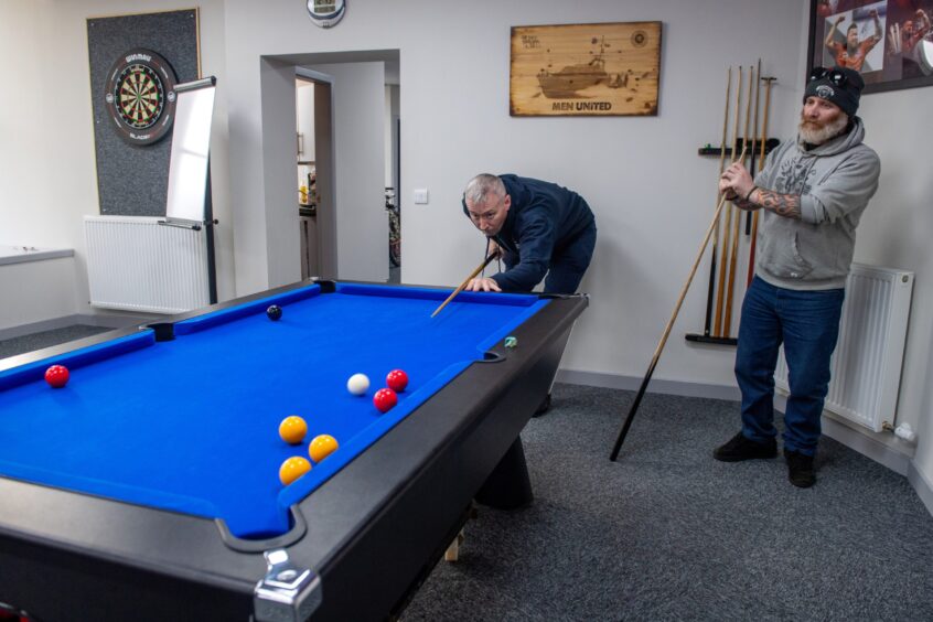Two men playing a game of pool in the Men United base in Peterhead.