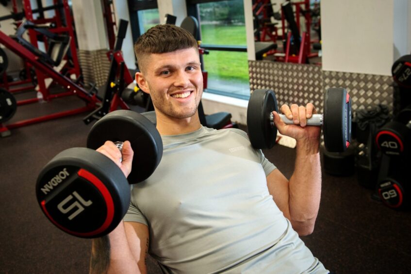 James Connelly smiling holding weights in each hand inside westhill gym Colosseum