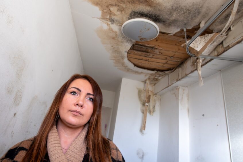 Aberdeen City Council tenant Karolina Osinska in her bathroom before the repair work, the ceiling is brown and black with damp and there is a section of plaster missing