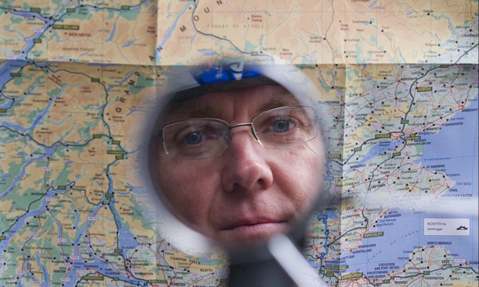 A reflection of Neil Innes in a bike mirror in front of a map