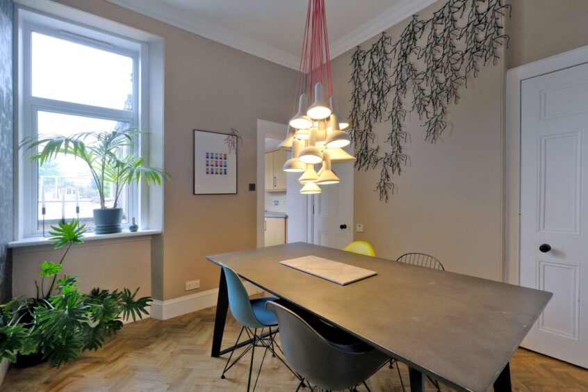 The dining area with a statement ceiling light, faux ivy on the walls, large houseplants next to the window and a modern table with four chairs