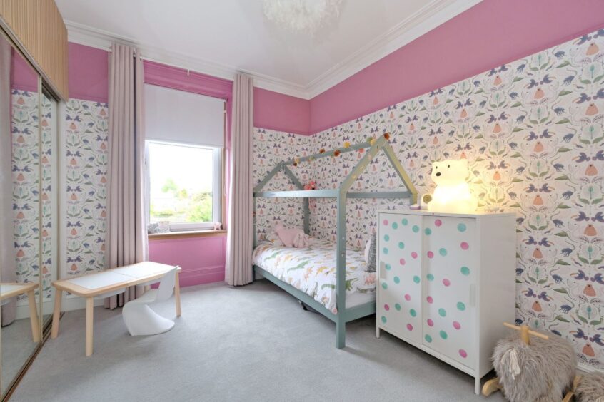 One of the childrens rooms in the house. It has a mirrored built-in wardrobe, floral wallpaper, a small drawing table, small white unit and a painted wooden-framed single bed