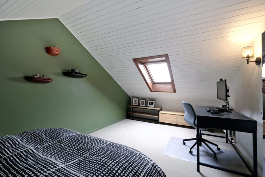 The master bedroom with slanted ceilings. There is a double bed, computer desk and chair and dark green feature wall
