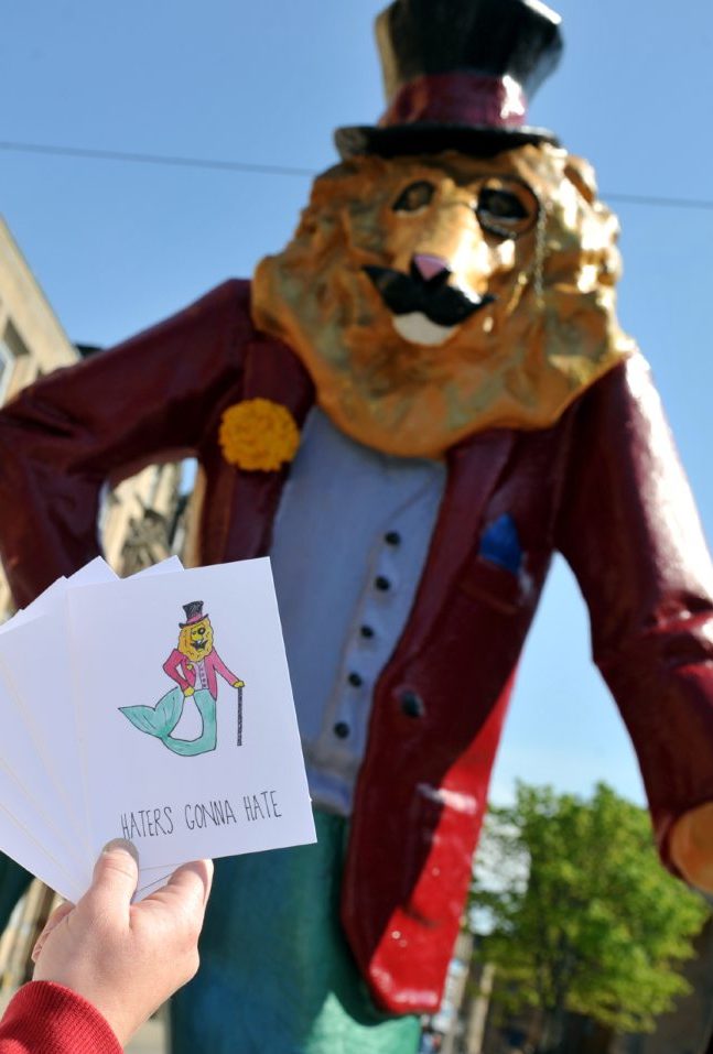 Someone holding cards inspired by Dandy Lion with the sculpture behind them