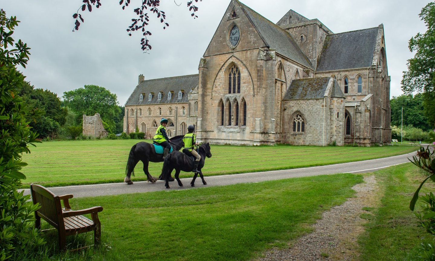 Exterior view of Pluscarden Abbey with horses on path. 