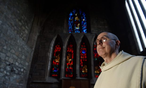 Brother Michael in the chapel at Pluscarden Abbey with stained glass window behind.