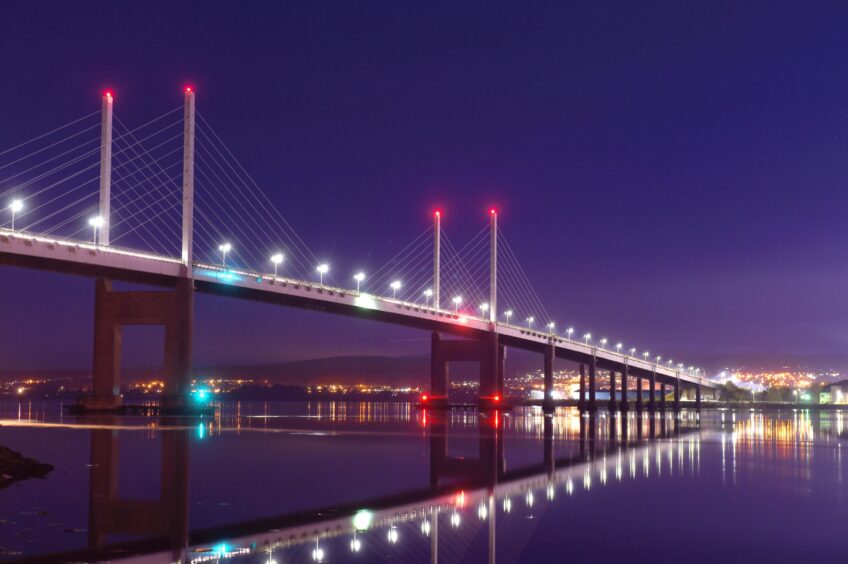 Lights from the Kessock Bridge reflect in the water below in the evening.
