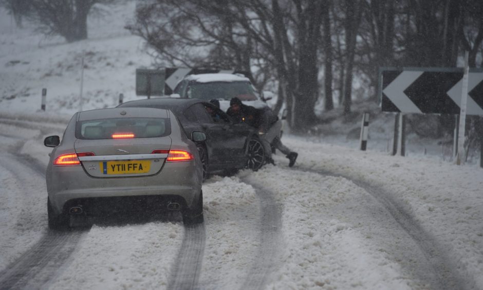 People pushing a car in the middle of the storm on the A9 near Dalwinnie
