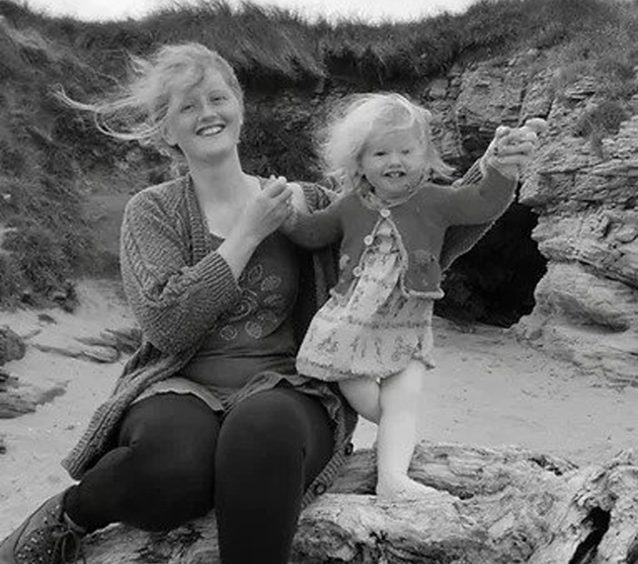 A black-and-white picture of a woman and her daughter laughing on the beach.