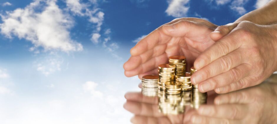 Hands include several stacks of coins in front of blue sky.