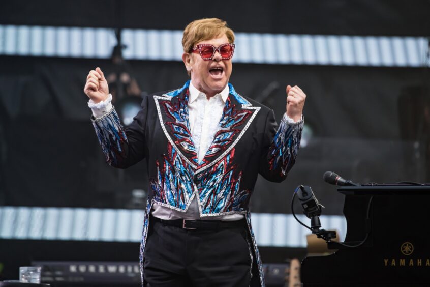 Elton John on stage cheering with two fists in the air. 