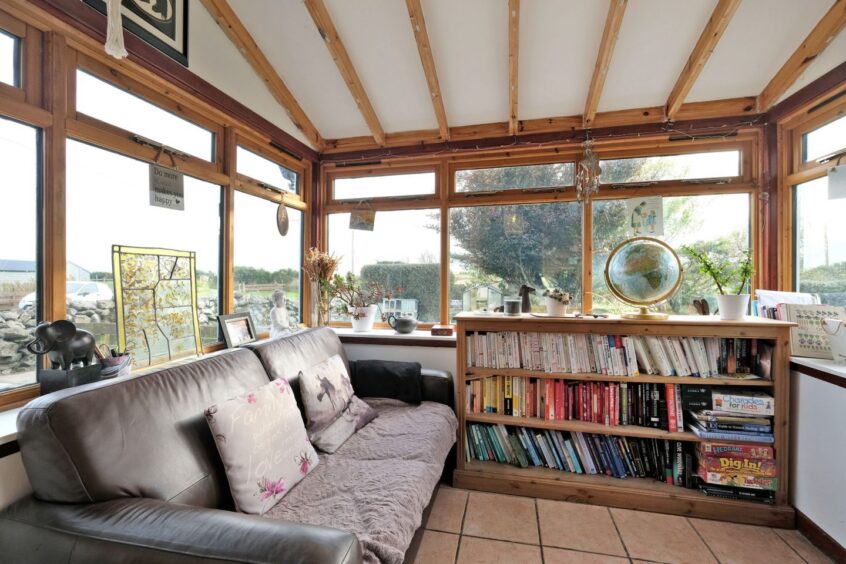 A conservatory-style room with a leather sofa and short, wide wooden bookcase - a perfect reading nook.