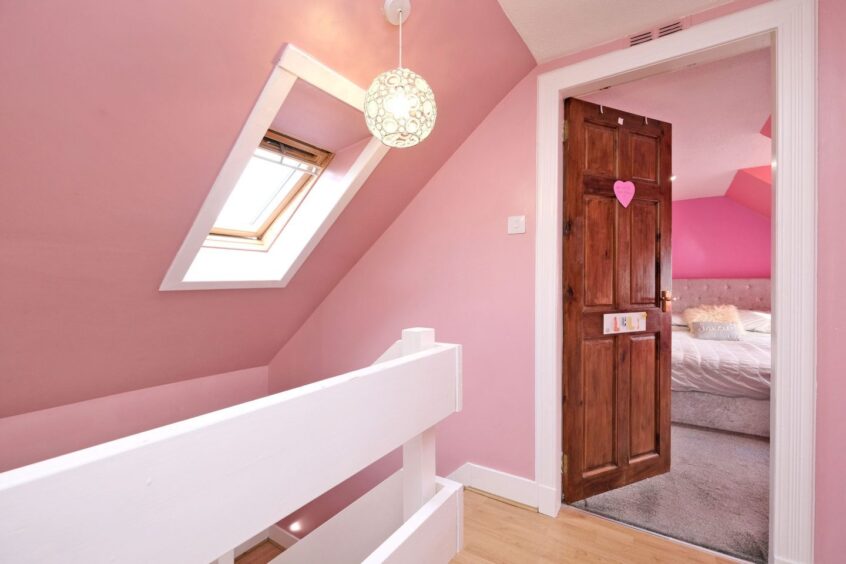 The hallway with a white bannister going down the stairs, the walls are painted a shade of rose pink