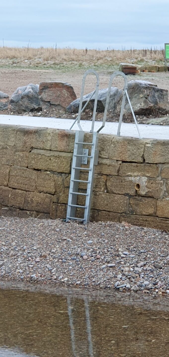 Ladder descends from pier into stones. 