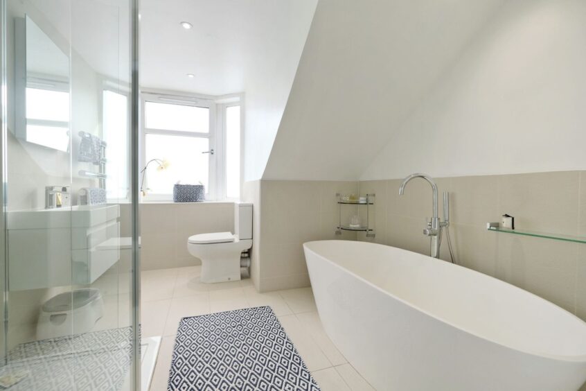 The bathroom is fitted with a toilet, oval-shaped bath, sink and walk-in glass shower cubicle. The walls are half white paint-half beige tile, matching the beige floor tiles
