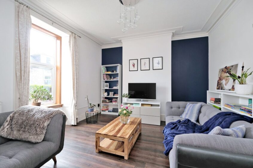The living room has wood-effect flooring, white and grey furnishings and dark blue accents