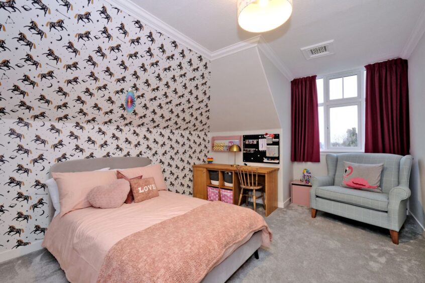 A bedroom in the home with a double bed, unicorn-print wallpaper accent wall, an armchair and desk
