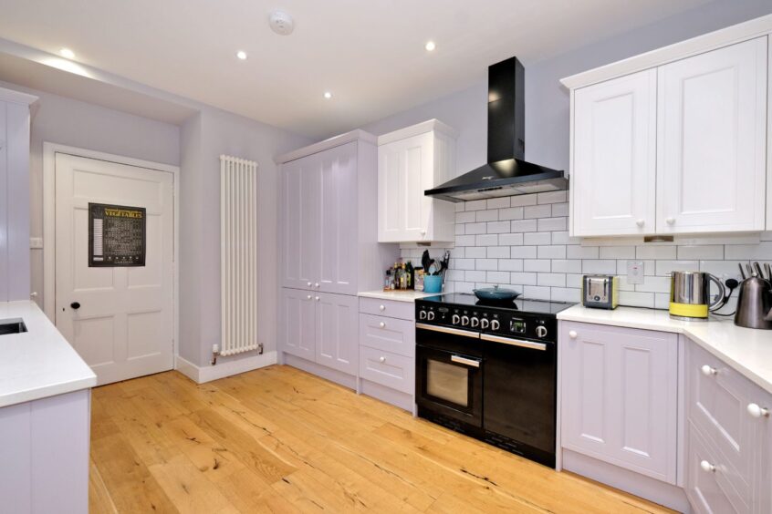 The kitchen in the Craigie Park Aberdeen home with wooden laminate flooring, pale grey walls and cupboards and white countertops