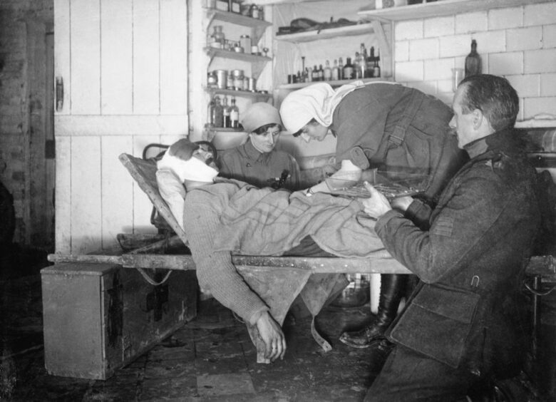 Elsie Knocker, assisted by Mairi Chisholm and a Belgian orderly operating on a wounded Belgian soldier in their first aid post in Pervyse, 1917.
