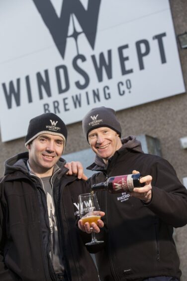 The two founders of Windswept Brewing Co outside their brewery holding beer. 