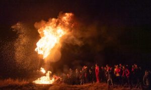 Flames reaching into the night sky as crowd looks on.