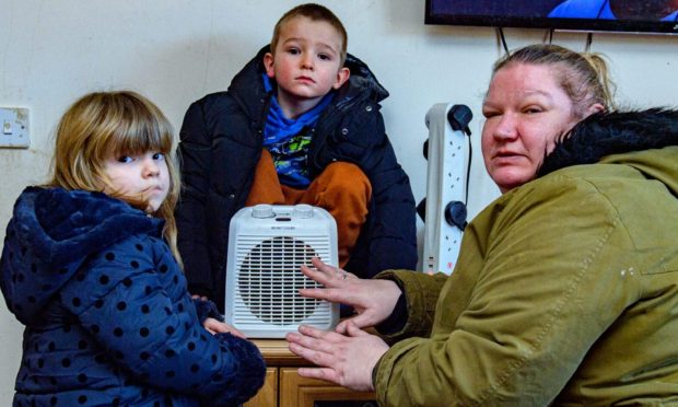 Laura Smith and two children around fan heater with TV in background.