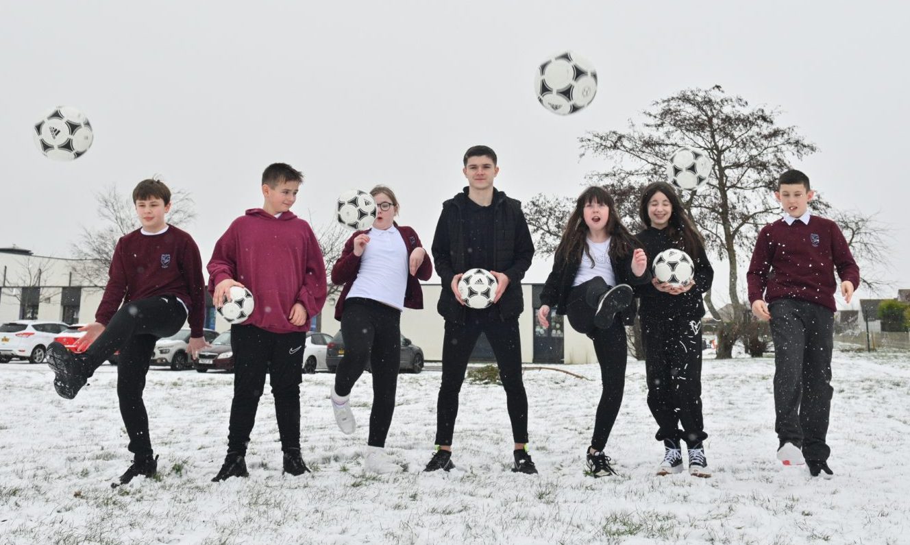 Marcus Goodall and school pupils in snow kicking footballs. 