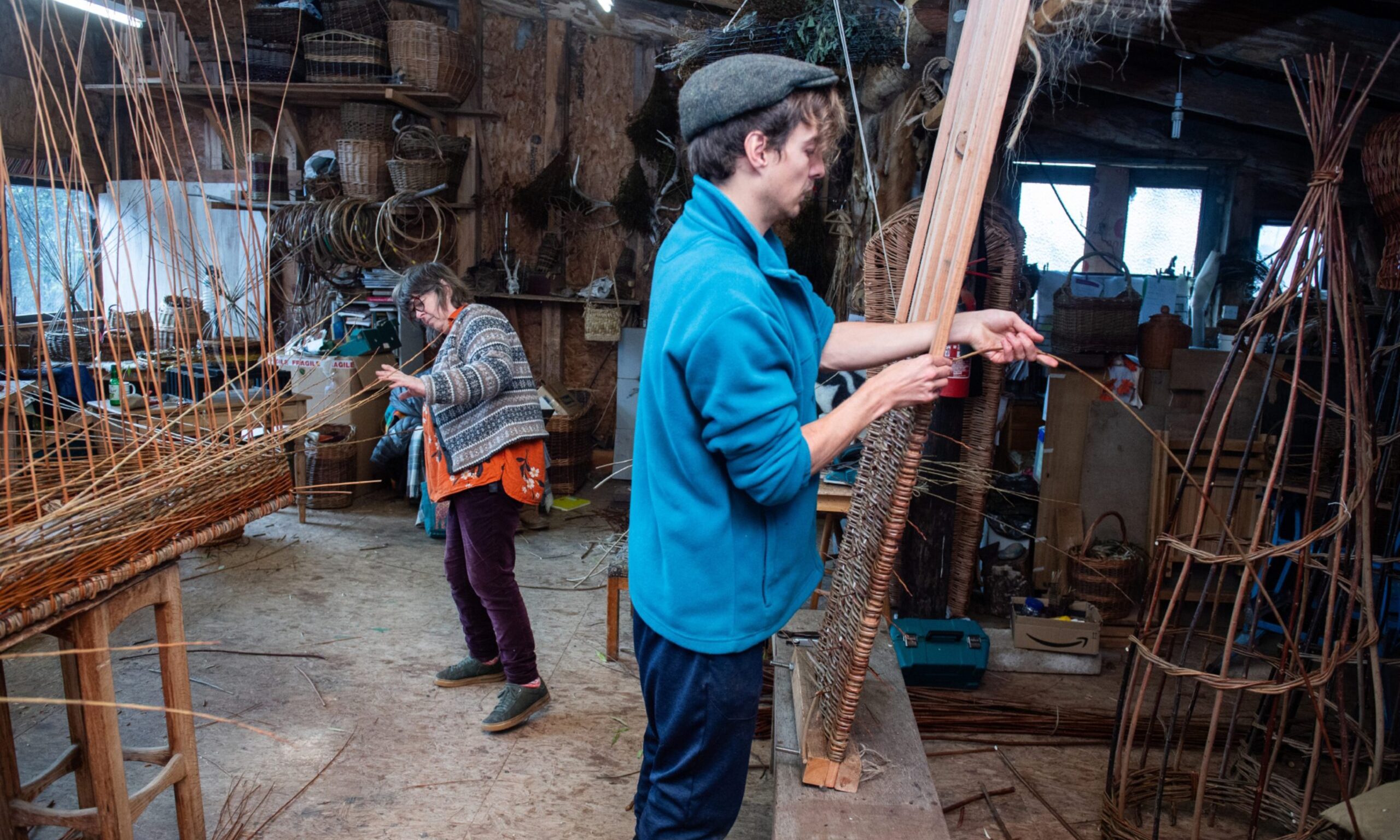 Two workers making willow coffins inside workshop. 