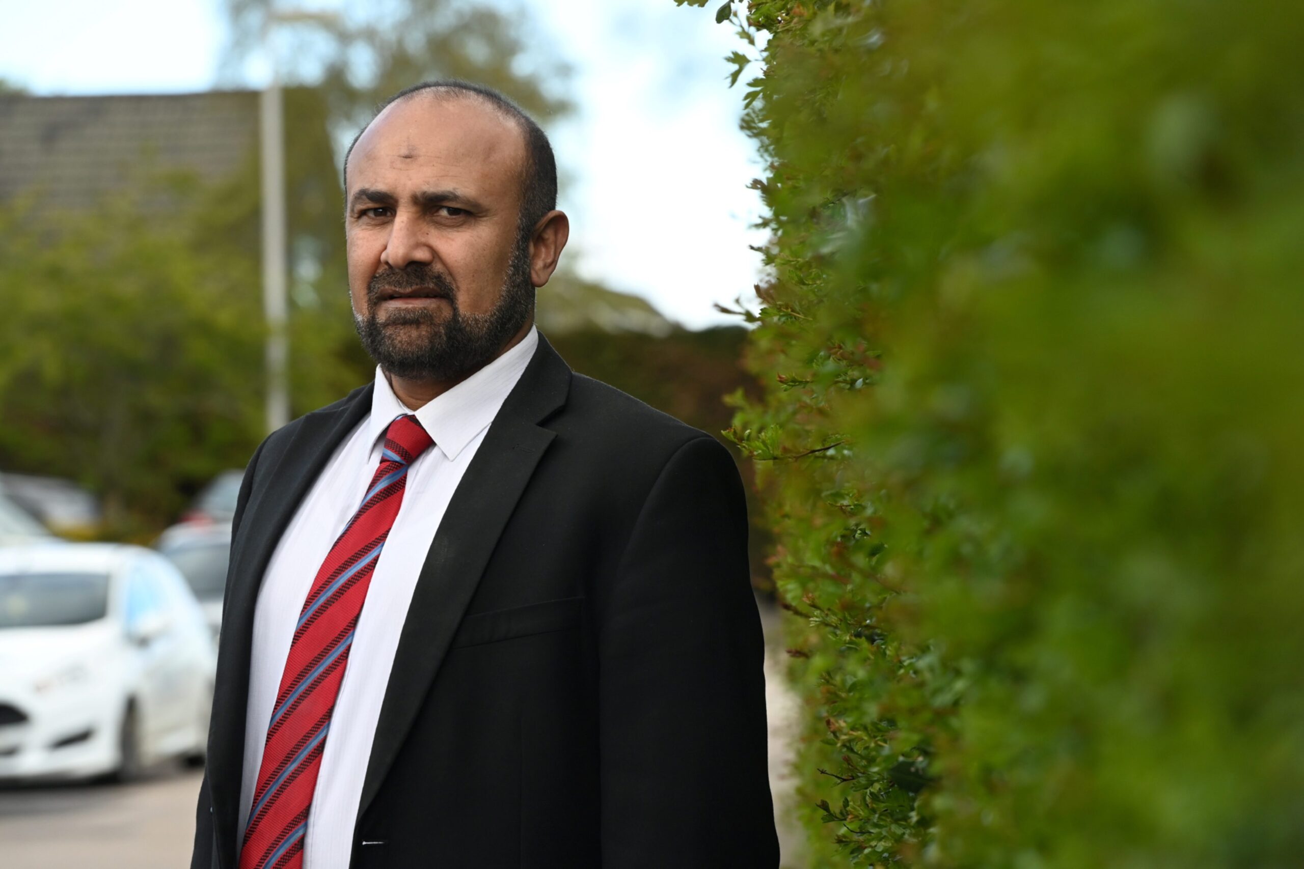 M. Tauqeer Malik leaning against a hedge.