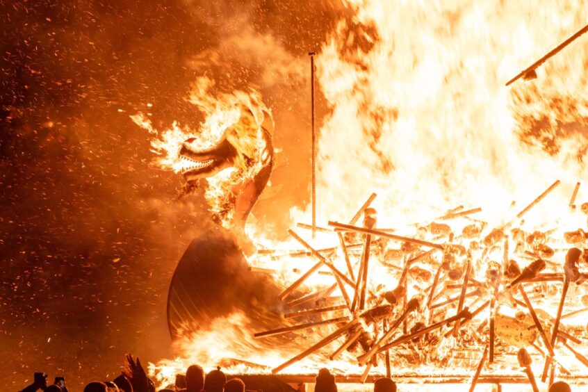 The burning dragon boat at Up Helly Aa 2024. Flames consume the masthead as the torches burn.