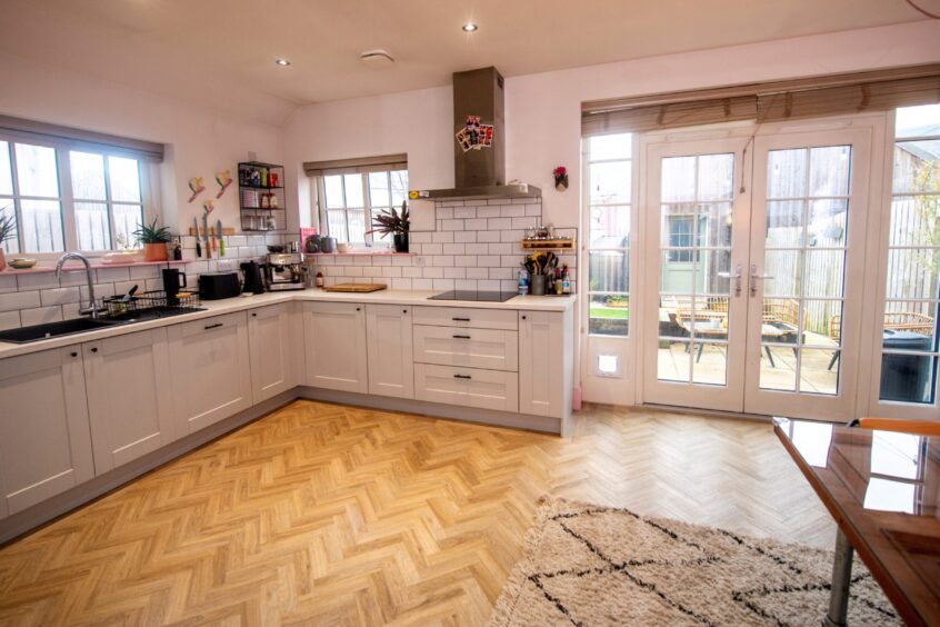 Spacious kitchen with white backsplash, black fixtures and herringbone wood flooring.