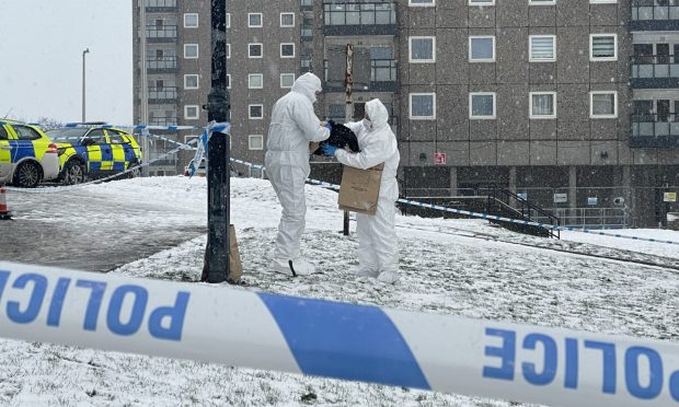 Forensic officers can be seen putting items in a bag outside the building.