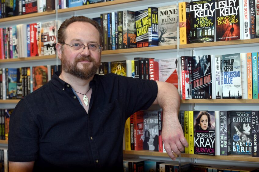 Stuart MacBride in Waterstones Aberdeen leaning on a bookshelf.