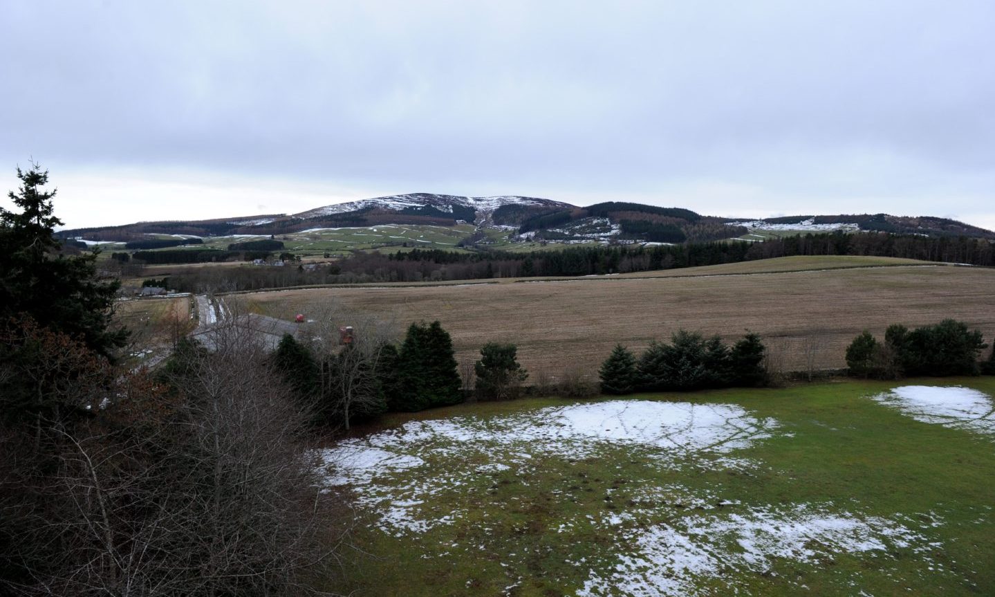 The view from the top of Tillycairn Castle during winter, with trees, snowy fields and hills in the distance