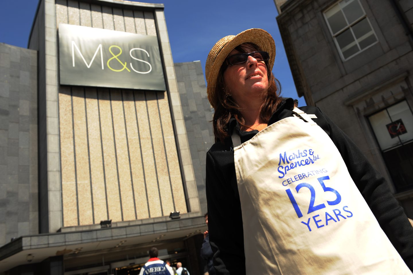 A woman in an apron reading "Marks & Spencer celebrating 125 years" outside the Aberdeen shop