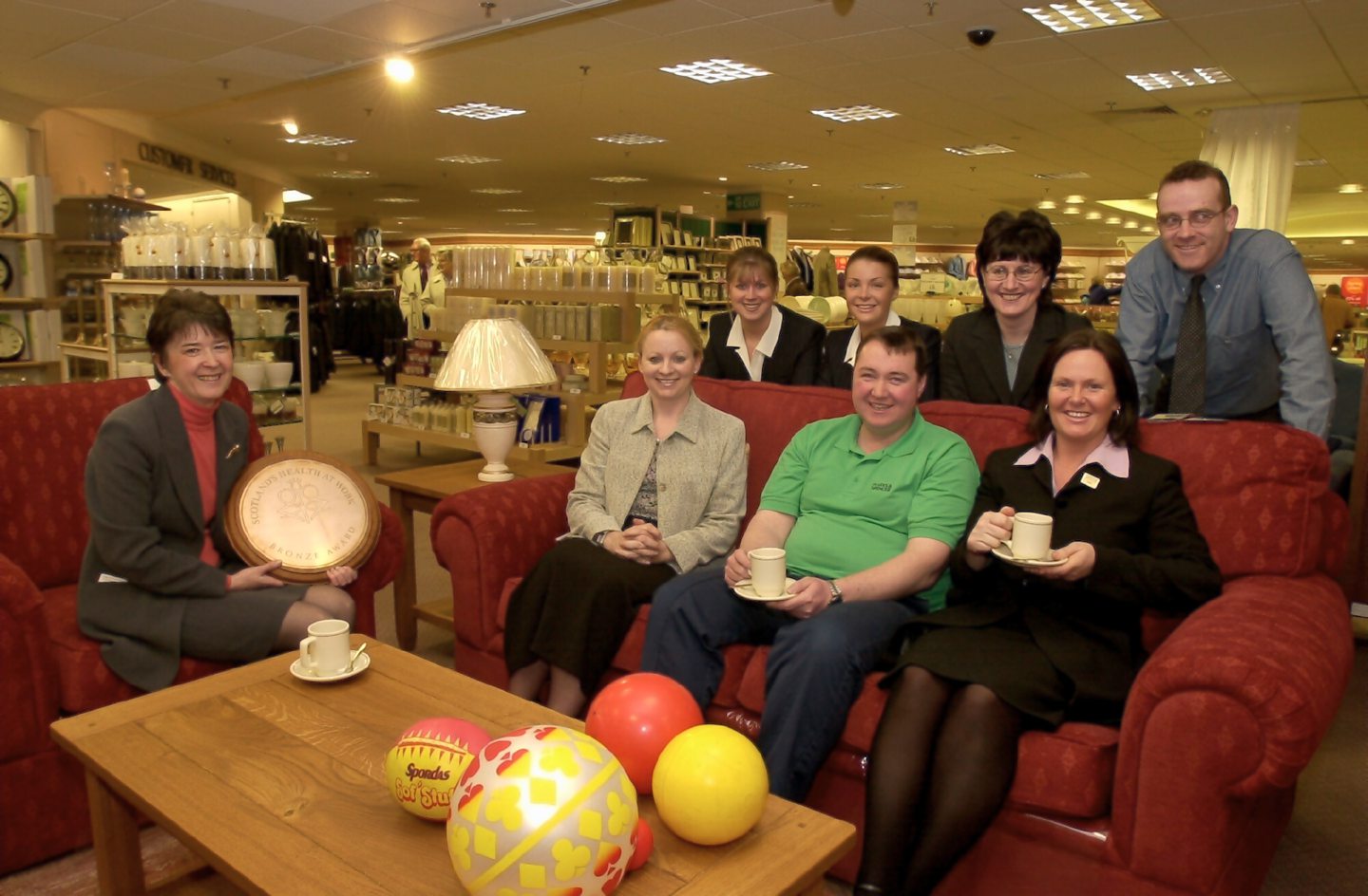 Some of Marks & Spencer staff sitting on and standing around a sofa and armchair set in the shop