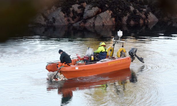 Staff onboard a small orange boat bring debris from the Strathan Bay.