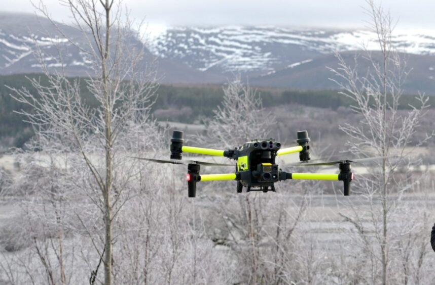 A yellow and black thermal imaging drone hovers in the air.