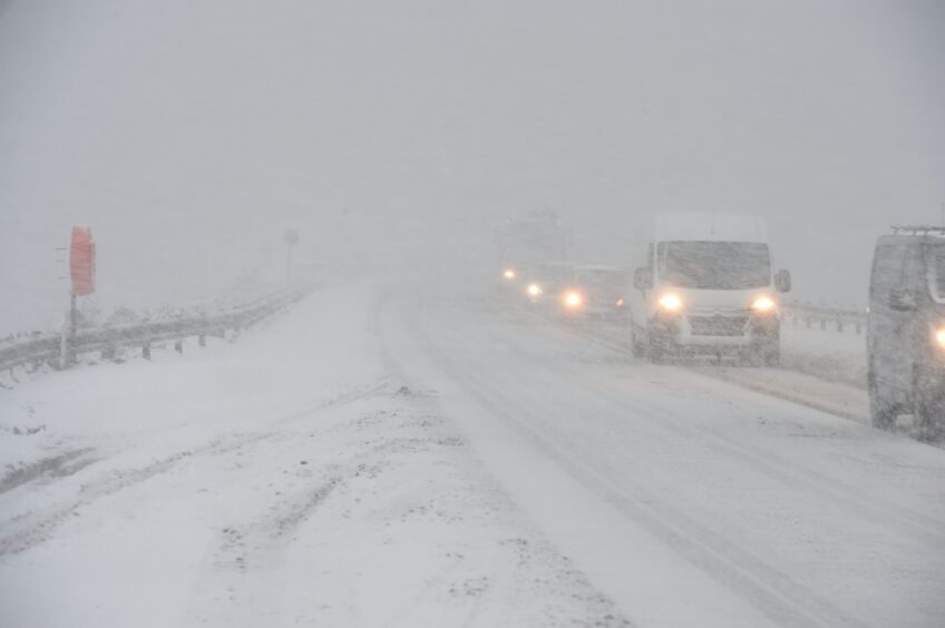 Vehicles with headlights on driving through snow on the A9 at Cromarty Bridge 