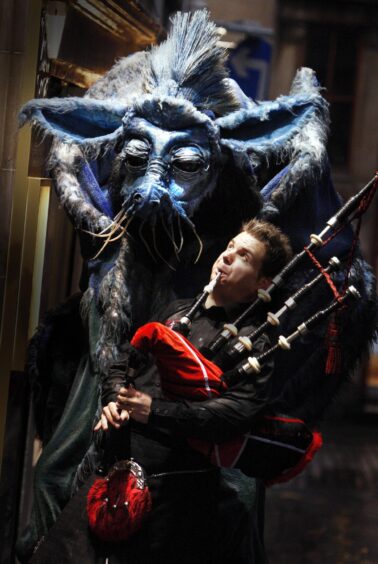 Stuart Cassells plays the pipes at a Hogmanay event in Edinburgh in 2007 in front of a puppet-like monster.