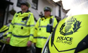 Police Scotland officers standing beside motorbike.