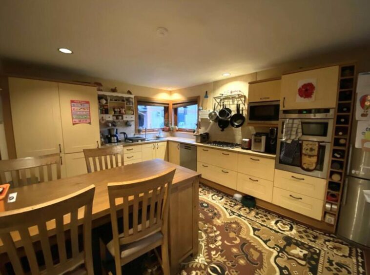 A dining table sits in the middle of a cream and brown designed kitchen.