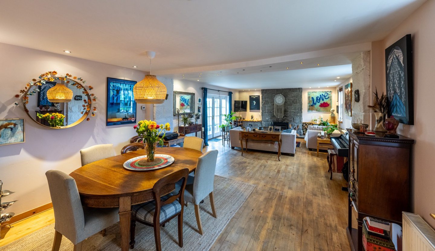A view of the open plan dining/sitting room from the dining area, there is a wooden dining table with six chairs, a round wall-mounted mirror and a cabinet