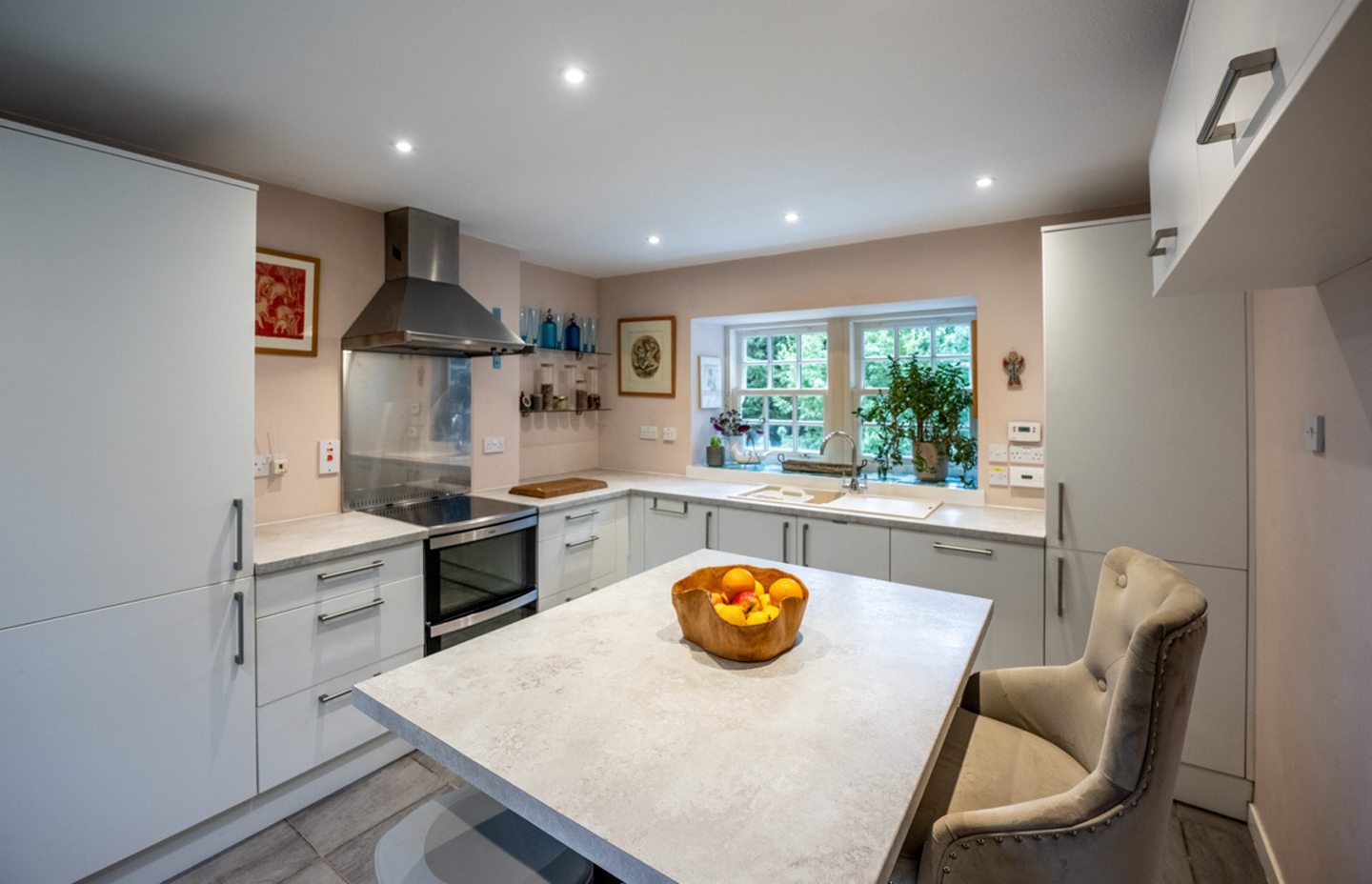 The kitchen in the lodge and creamery in Torphins which features white cabinets, cream marble countertops, steel and black oven with a hood and a kitchen island with barstools
