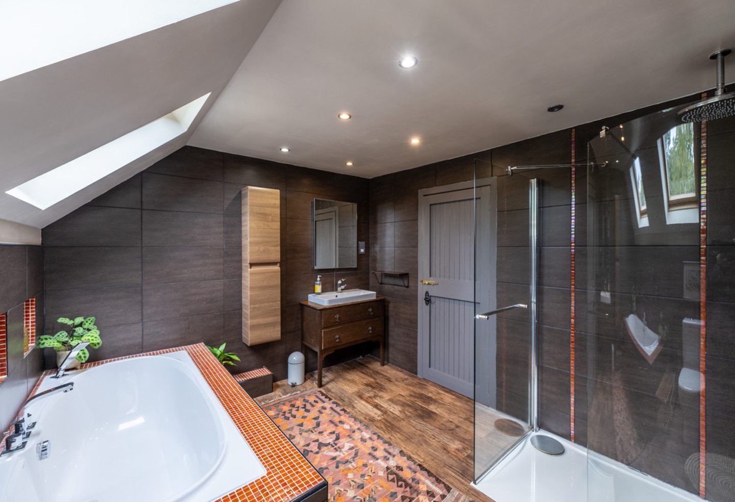 The bathroom in the lodge and creamery in Torphins with dark wood tones, orange tiled accents, on the walls and sinks