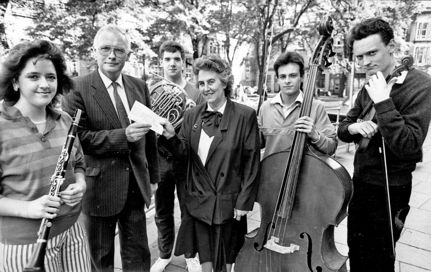 Manager, Bill Neish handing a cheque to Dorothy Hately, secretary/treasurer for the North East of Scotland Music School, surrounded by young people with instruments