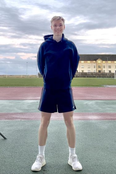 Runner and Strava user Max Abernethy stands on an athletics track looking at the camera