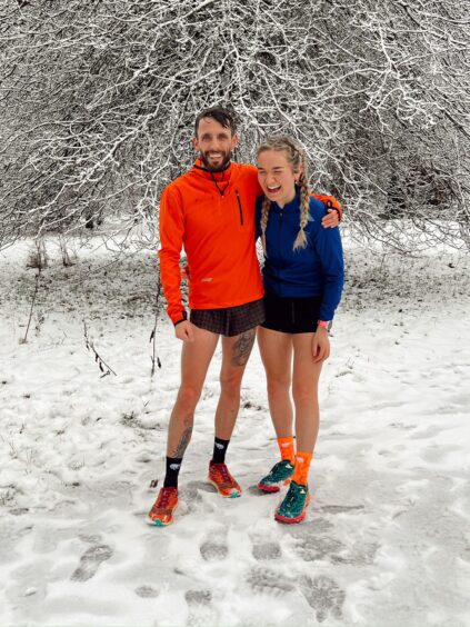 Runner and Strava user Rosie Dunlop laughs in the snow with her boyfriend while wearing running gear.